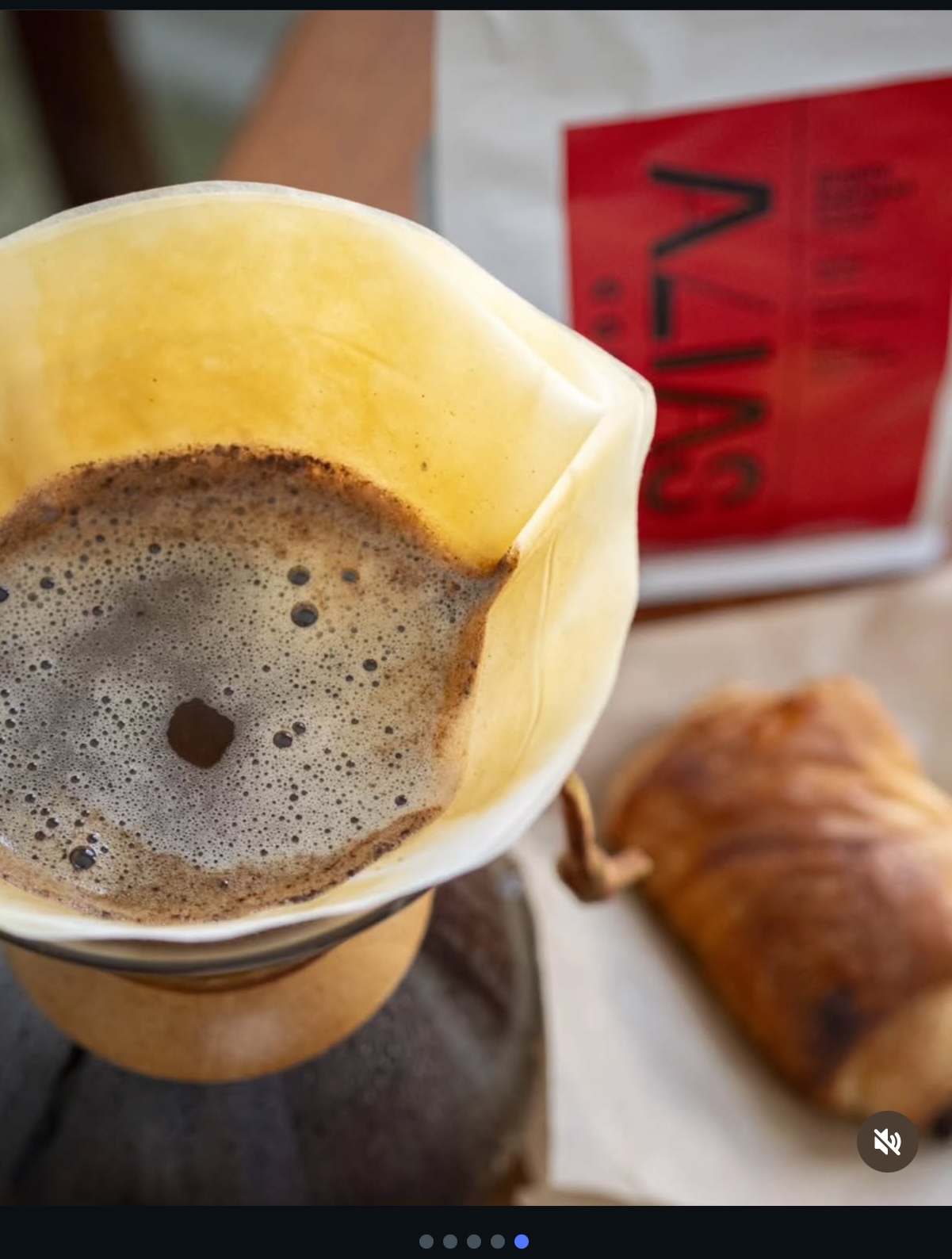 Espresso pouring from a spout of a machine into two small white-inlined cups